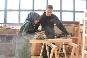 Young refugee woman uses tools in the wood workshop of makerspace Habibi.Works